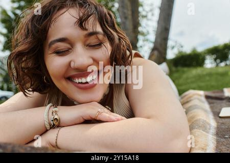 Eine fröhliche junge Frau entspannt sich auf einer Decke, während sie sich in der Wärme eines sonnigen Picknicks im Sommer sonnt. Stockfoto