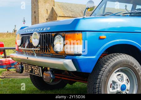 Nahaufnahme eines klassischen blauen Range Rover, der auf einem grasbewachsenen Feld in der Nähe eines historischen Steingebäudes parkt. Stockfoto