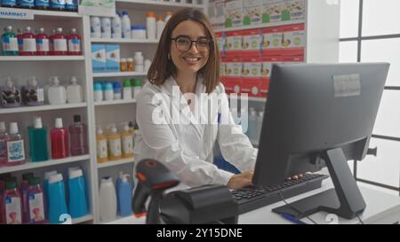 Attraktive hispanische Frau, die in einer Apotheke arbeitet, Laborkittel und Brille trägt, die Kamera hinter einer Theke in einer Drogerie mit Medikamenten lächelt Stockfoto