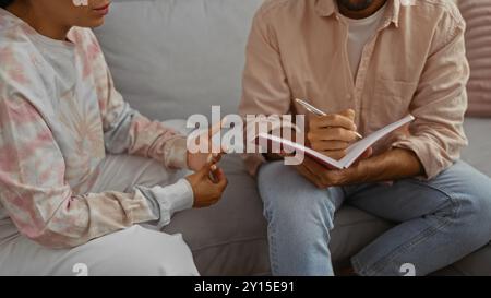 Frau, die mit einem Mann spricht, mit einem Notizbuch zu Hause, das eine ungezwungene und informelle Umgebung in einem Wohnzimmer zeigt, die ihre Beziehung und Inter demonstriert Stockfoto