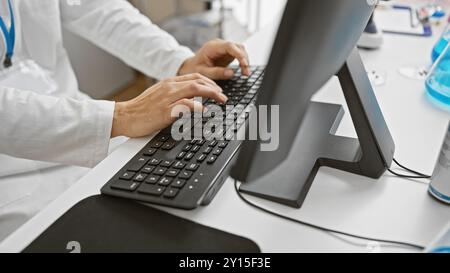 Nahaufnahme der Hände eines Mannes, die auf einer Tastatur in einem modernen Labor tippen, was die Forschung im Gesundheitswesen oder die Dateneingabe anzeigt. Stockfoto