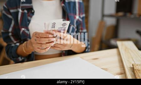 Die junge asiatin zählt isländische Kronen in einem Holzbearbeitungsstudio. Stockfoto