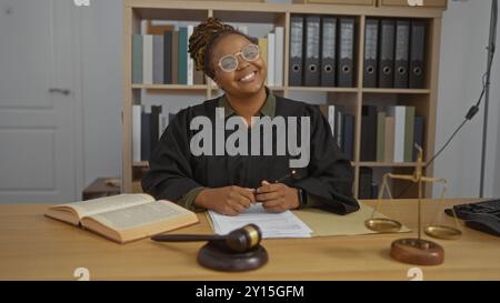 Lächelnde Richterin mit Brille im Gerichtssaal mit juristischen Büchern und Waagen Stockfoto
