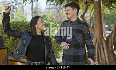 Ein glückliches Paar tanzt fröhlich auf einer städtischen Straße und zeigt Liebe und Gemeinschaft mit einem Hintergrund von Palmen. Stockfoto