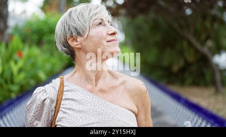 Eine besinnliche reife hispanische Frau mit kurzen grauen Haaren genießt Ruhe in einem üppig grünen Park. Stockfoto