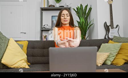 Frau, die während einer Pause vom Laptop Arme streckt, arbeitet in einem gemütlichen Wohnzimmer mit Gitarre und Pflanzen. Stockfoto