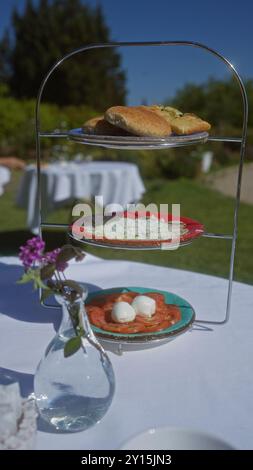 Outdoor-Dining-Szene mit verschiedenen Vorspeisen auf einem gestuften Tablett, umgeben von üppigem Grün und einem klaren blauen Himmel, schaffen ein malerisches Restaurant Stockfoto