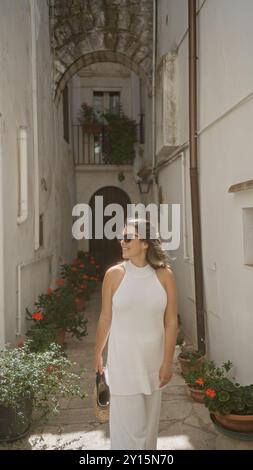 Eine junge hispanische Frau schlendert durch die wunderschönen Straßen der Altstadt in locorotondo, apulien, italien, und bewundert die bezaubernden weißen Gebäude und Stockfoto