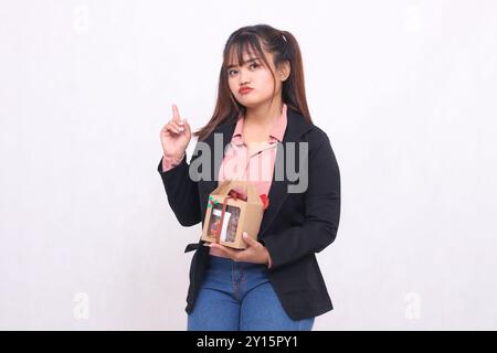 Schönes asiatisches Mädchen in ihren 20ern, das aufgeregt weihnachtliches Geschenk in Form von Korb in der Hand auf weißem Hintergrund für Werbematerial zeigt Stockfoto
