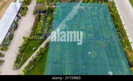Luftaufnahme einer Gartenanlage mit verschiedenen Pflanzen und Bäumen unter Schutznetz. Wege trennen Abschnitte des Grüns und zeigen eine Vielfalt Stockfoto