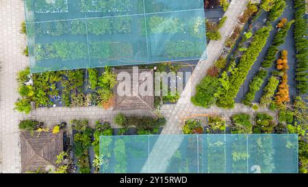 Luftaufnahme einer Gartenanlage mit verschiedenen Pflanzen und Bäumen unter Schutznetz. Wege trennen Abschnitte des Grüns und zeigen eine Vielfalt Stockfoto
