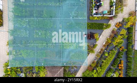 Luftaufnahme einer Gartenanlage mit verschiedenen Pflanzen und Bäumen unter Schutznetz. Wege trennen Abschnitte des Grüns und zeigen eine Vielfalt Stockfoto