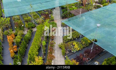 Luftaufnahme einer Gartenanlage mit verschiedenen Pflanzen und Bäumen unter Schutznetz. Wege trennen Abschnitte des Grüns und zeigen eine Vielfalt Stockfoto