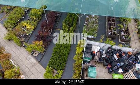 Luftaufnahme einer Gartenanlage mit verschiedenen Pflanzen und Bäumen unter Schutznetz. Wege trennen Abschnitte des Grüns und zeigen eine Vielfalt Stockfoto