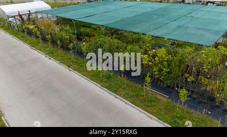Luftaufnahme einer Gartenanlage mit verschiedenen Pflanzen und Bäumen unter Schutznetz. Wege trennen Abschnitte des Grüns und zeigen eine Vielfalt Stockfoto