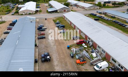 Eine Luftaufnahme eines Gewerbegebiets mit mehreren Gebäuden, geparkten Fahrzeugen und verstreuten Baumaterialien. Die Szene enthält eine Mischung aus ca. Stockfoto