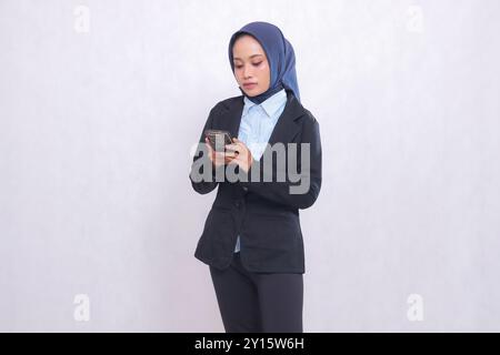 Asiatische Büroleiterin mit Hijab steht elegant und bedient ihr Handy. Schöne muslimische Frau in blauem Hemd für Geschäfte und Finanzen Stockfoto