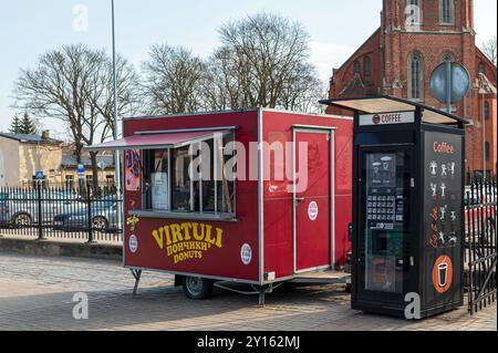 Liepaja, Lettland - 19. März 2023: Ein lebhafter Food Truck, der Donuts verkauft, steht bei Tageslicht neben einem Kaffeekiosk. Stockfoto