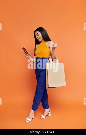 Eine modische Frau überprüft ihr Handy, während sie Einkaufstaschen trägt. Stockfoto