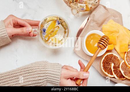 Frau fügt Honig zu einer Bio-Bergmischung hinzu – erfrischendes Kräuteraufguss-Konzept. Stockfoto