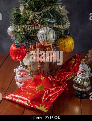 Nahaufnahme eines kleinen, geschmückten Weihnachtsbaums mit einem Geschenk und Weihnachtsmannfiguren darunter Stockfoto