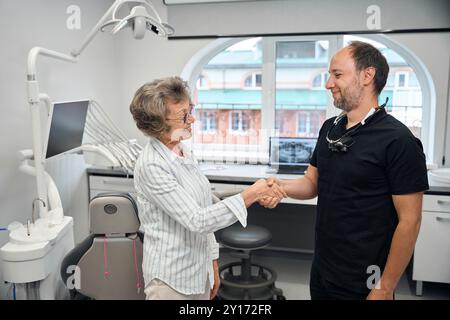 Ein Spezialist begrüßt eine ältere Dame mit einem Handschlag Stockfoto