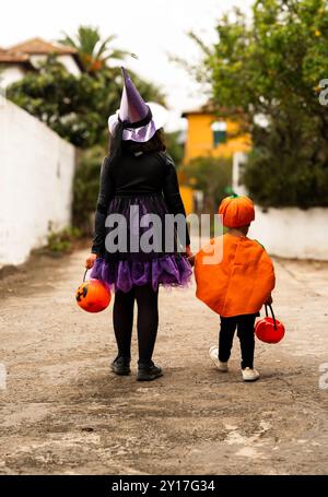 Eine Frau und ein Kind laufen in Halloween-Kostümen die Straße entlang. Die Frau trägt ein schwarzes Kleid und einen lila Hut, während das Kind W ist Stockfoto