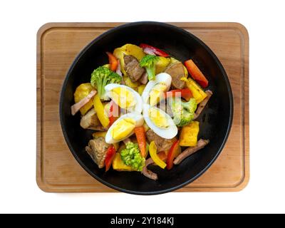 Buntes herzhaftes Rühren mit Gemüse und gekochtem Ei in Skillet auf Holzbrett. Stockfoto