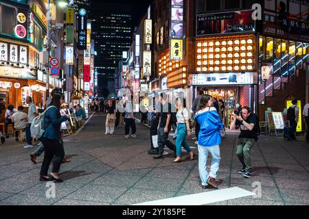 Tokio, Japan, 14. Juni 2024: Besucher spazieren durch die Straßen der Stadt Shinjuku, einem großen Handels- und Verwaltungszentrum, während einer Sommernacht mit Schildern Stockfoto