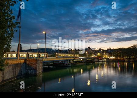 03-09-2024 Zürich, Schweiz. Quaibrücke oder Quai Brücke über die Limmat bei Sonnenaufgang. Leichter Brückenverkehr, Straßenbahnen, dramatischer Himmel, Reflexionen Stockfoto