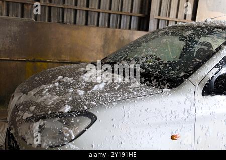 Ein Auto wird in einer automatisierten Autoreinigungsanlage gründlich gewaschen, die mit Schaumseife bedeckt ist, während Wasser aus verschiedenen Winkeln spritzt. Stockfoto