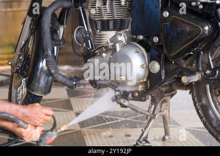 Eine Person verwendet einen Hochdruckreiniger, um den Motor eines Motorrads zu reinigen und stellt sicher, dass er in der frühen Zeit an einer Motorradreinigungsstation frei von Schmutz und Schmutz ist Stockfoto