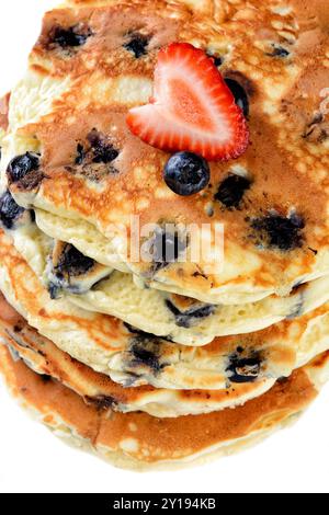 Nahaufnahme eines Stapels frischer hausgemachter Heidelbeerpfannkuchen mit einer Erdbeere auf weißem Teller und rustikalem Holztisch. Stockfoto