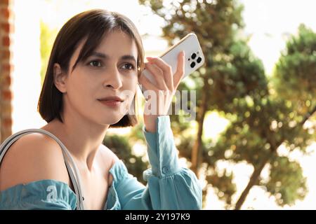 Schöne Frau mit Smartphone, die draußen Sprachnachrichten hört Stockfoto