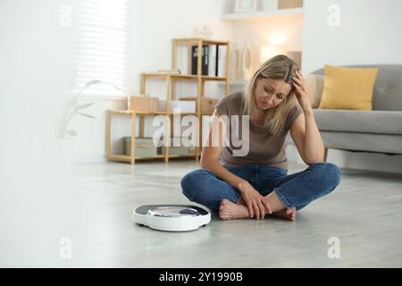 Wechseljahre, Gewichtszunahme. Besorgte Frau, die zu Hause in der Nähe der Waage sitzt Stockfoto