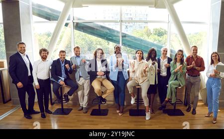 Eine Gruppe von Geschäftsleuten, die im Büro stehen und fröhlich auf die Kamera blicken und lächeln. Stockfoto