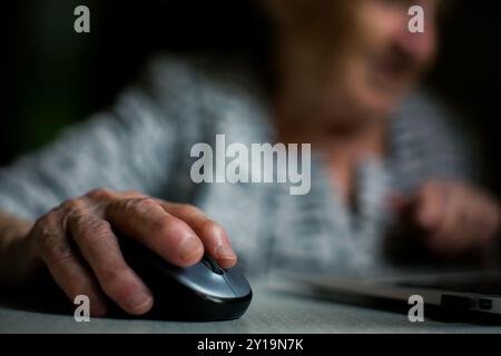 Nahaufnahme der Hand einer älteren Frau, die sanft auf einer Computermaus liegt, während sie mit Technologie arbeitet. Stockfoto