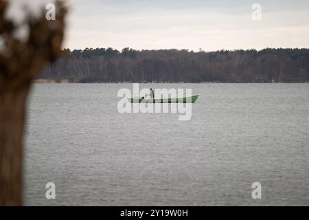 Angler, der im Winter allein auf einem kleinen Boot auf einem See steht. Fischer in der Natur und Entspannung während einer Outdoor-Aktivität. Stockfoto