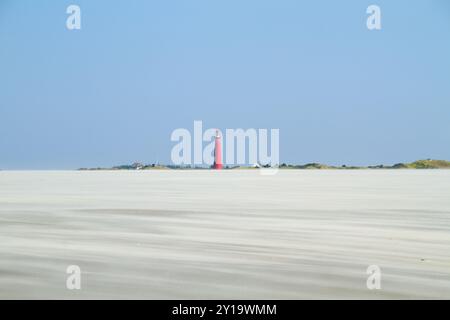 Blick auf einen riesigen Strand mit treibendem Sand, der durch starken Wind auf dem roten Leuchtturm der niederländischen Insel Schiermonnikoog verursacht wird Stockfoto