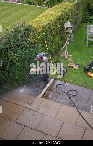 Ein Mann, der eine Terrasse in einem Garten oder Garten mit einem Hochdruckreiniger reinigt Stockfoto