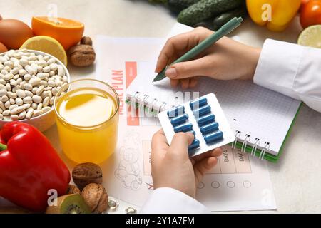 Ernährungsberaterin schreibt in Notizbuch und hält Pillen in der Nähe von gesundem Essen auf dem Tisch Stockfoto