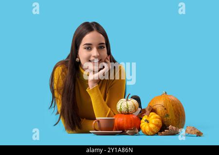 Schöne junge glückliche Frau mit Kürbissen, Herbstblättern und einer Tasse Tee, die auf blauem Hintergrund liegt Stockfoto