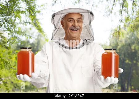 Glücklicher männlicher Bienenhalter in Uniform mit Honiggläsern und lächelndem Lächeln Stockfoto