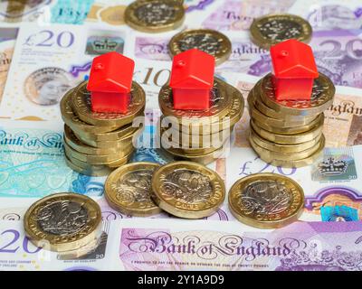 Nahaufnahme von Häusern aus Kunststoff, die auf Stapeln von britischen Pfund-Münzen und Pfund-Banknoten platziert wurden, Geld Bargeld, Großbritannien Stockfoto
