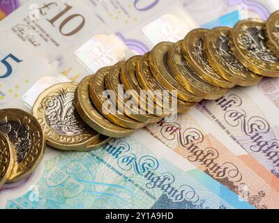 Nahaufnahme vieler britischer Pfund-Münzen, die auf Pfund-Banknoten liegen, Bargeld, Großbritannien Stockfoto