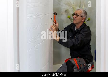 Installation eines Schlosses an der Holztür. Zimmermann, der Verriegelungsgriffe in der Zimmertür installiert Stockfoto