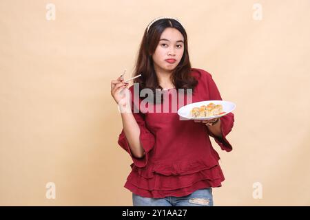 Die schöne junge indonesienfrau in rotem mürrisch trägt vorne einen Teller mit Dimsum (chinesisches Essen) und Sauce mit Essstäbchen. Wird für Lebensmittel verwendet Stockfoto