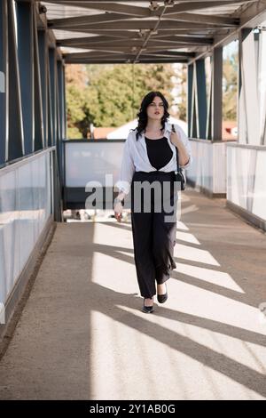 Selbstbewusste professionelle Frau, die auf einem erhöhten Walkway in sonnendurchfluteter städtischer Umgebung läuft. Stockfoto