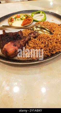 Porträt von Nasi Kebuli Ayam (Hühnerkebuli-Reis) in der Mitte mit Gurken, Sauce und Löffel, typisch arabisches Essen hergestellt in Indonesien auf dem t Stockfoto