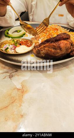 Porträt der Hand einer asiatischen Frau, die ein Gericht mit Löffel und Gabel auf einem Teller mit typisch arabischem Nasi-Kebuli (Reiskebuli) essen will Stockfoto